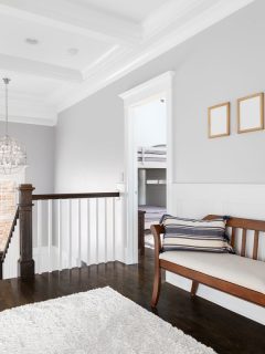 An upstairs hallway in a luxury home with a coffered ceiling, dark hardwood floor, a wooden bench, and board and batten walls, What's The Best Paint For Board And Batten?