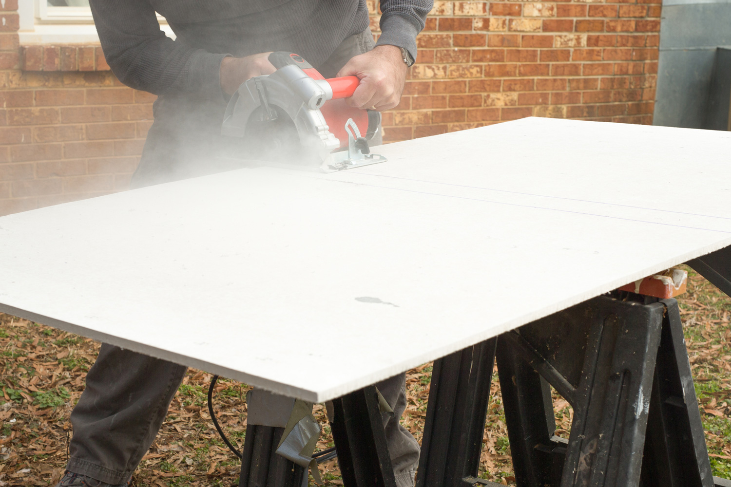 As the circular saw blade cuts into the cement board, dust creates clouds.