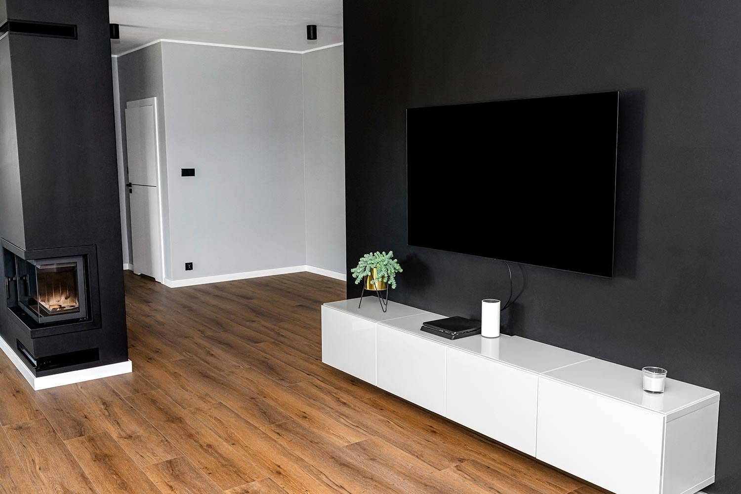 Black matte TV wall in the living room with a standing TV set on a white hanging cabinet