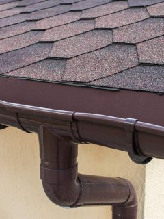 A brown plastic drainage on the roof near the shingles, What Color To Paint Gutter And Downspouts? [8 Options]