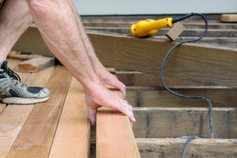 Carpenter installing new wood decking - How Much Space Between Deck Boards