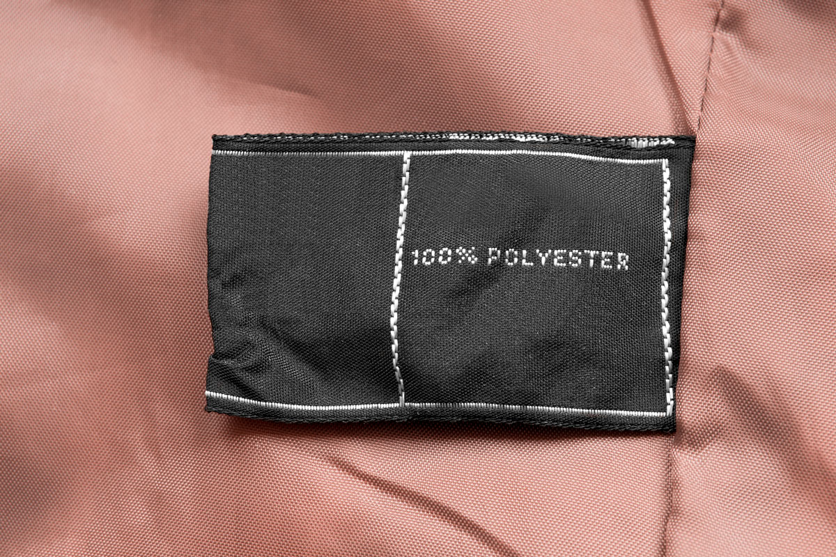 Clothes label says 100% polyester on beige textile background