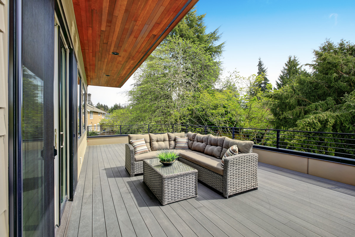 Contemporary deck features a modern wicker sectional accented with gray seat cushions facing a wicker coffee table. 
