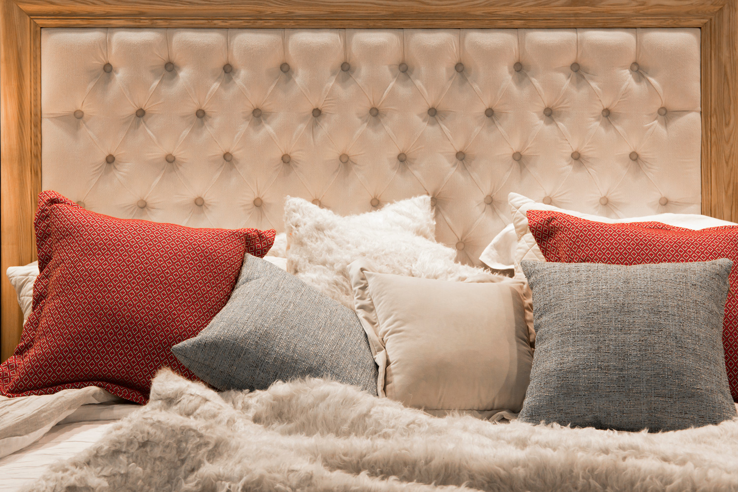 Cozy bed with quilted leather headboard in a wooden frame in beige and brown colors and pastel pillows.