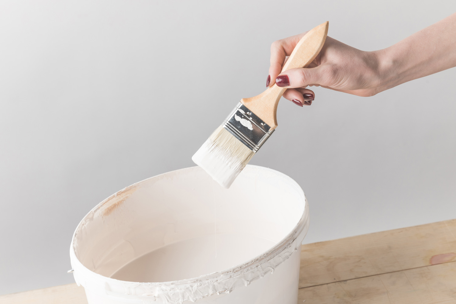 Cropped image of woman holding brush in white paint above bucket — Photo