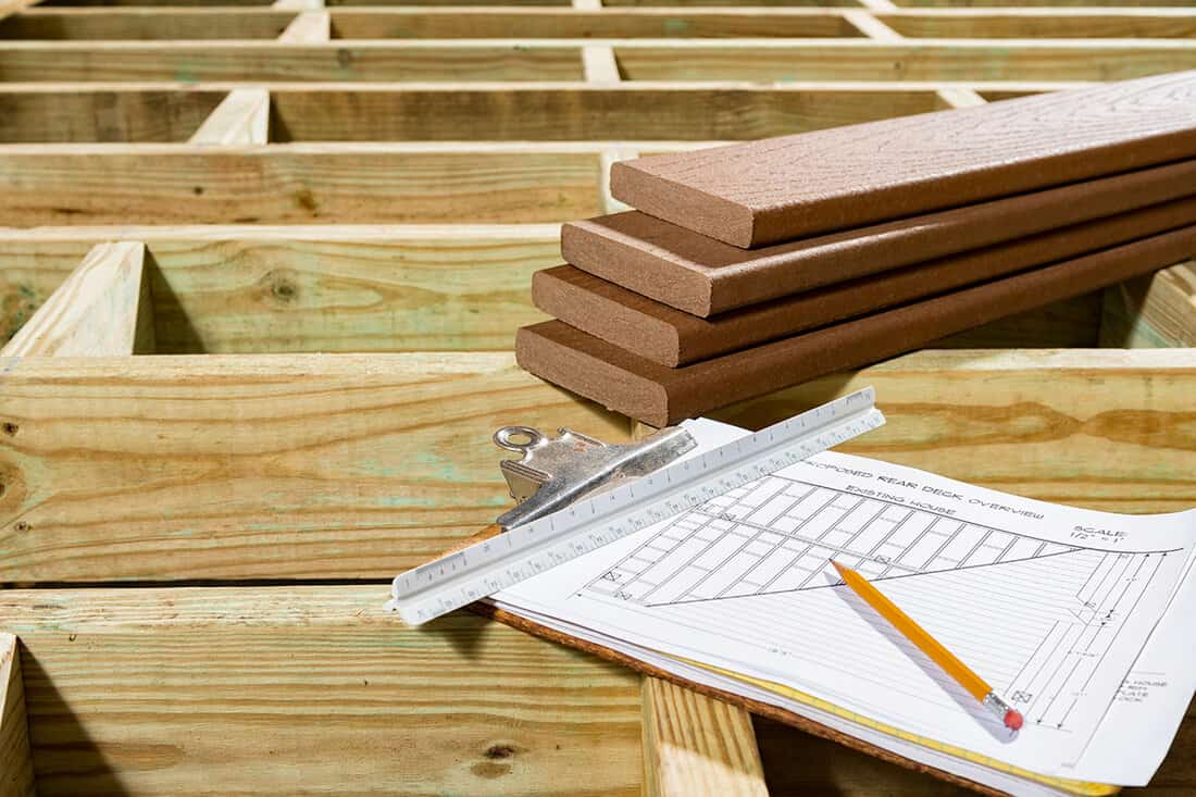 Deck plans in clipboard sitting on joist of pressure treated lumber