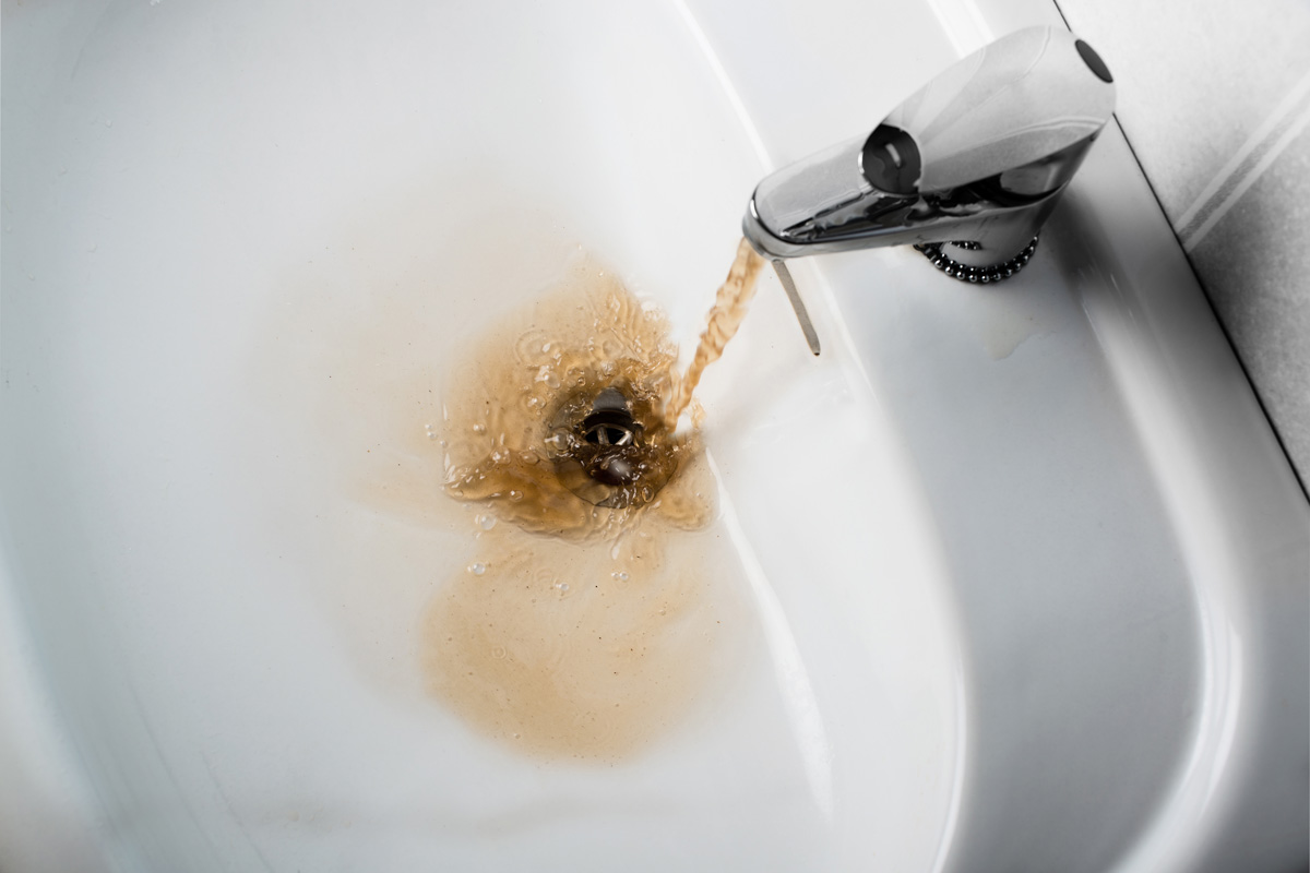 Dirty brown water running into a white sink. Looks very unhealthy,