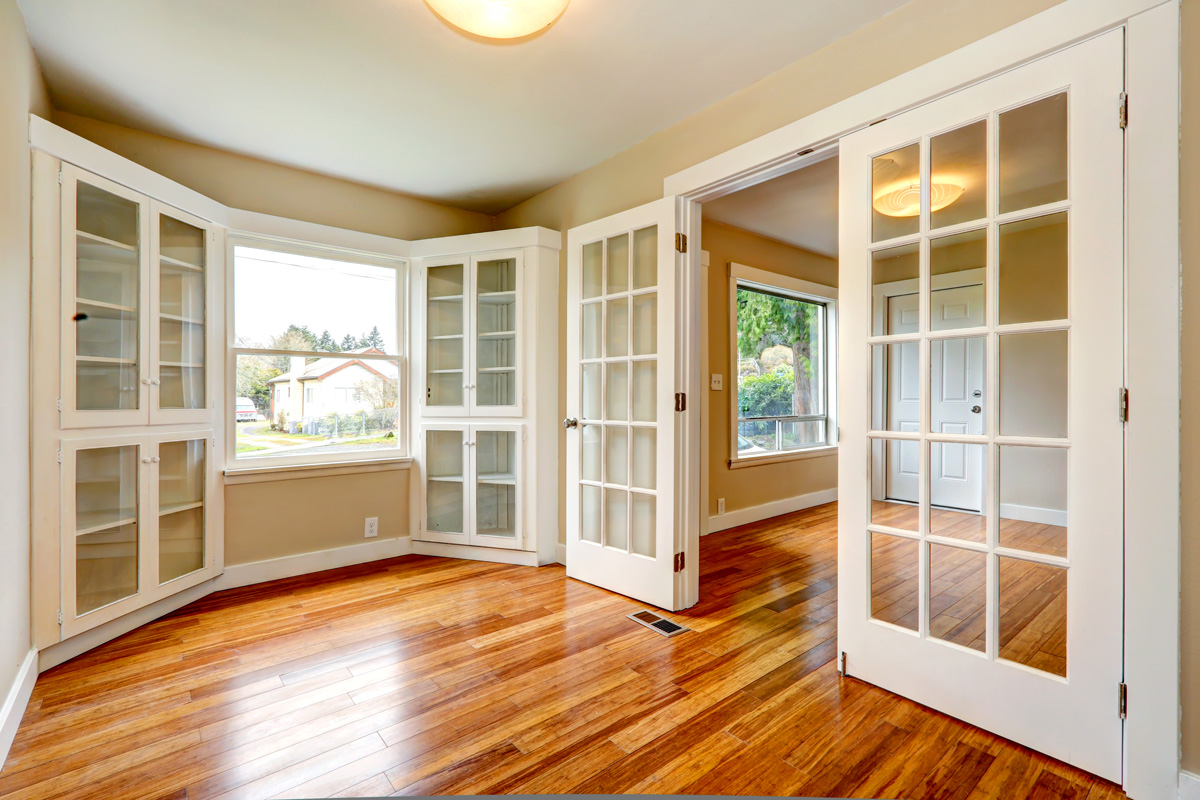 Empty house with new hardwood floor and white french doors. View of entrance hallway and small office room