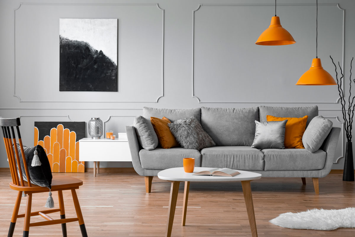 Gorgeous gray painted walls and a matching gray sofa with orange pillows and wooden furniture's