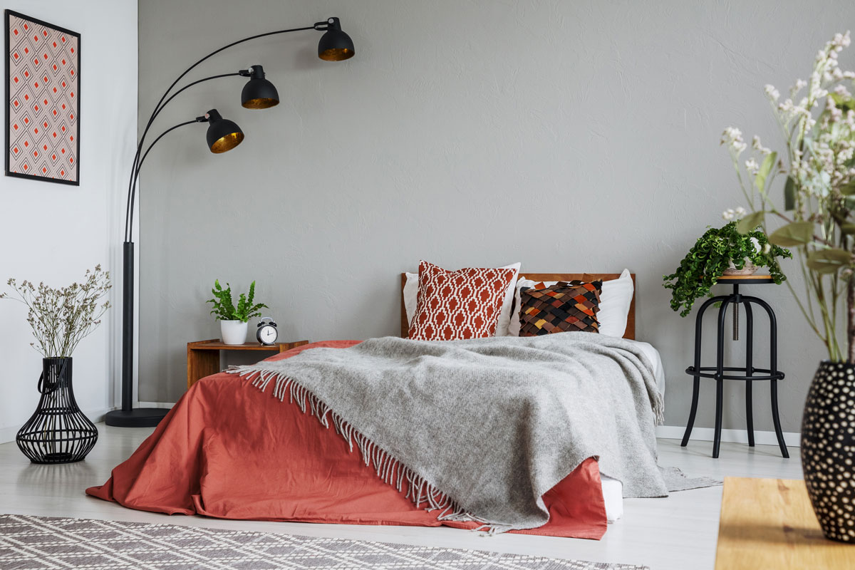 Gray colored bedroom wall with a three bulb hanging lamp with red colored beddings and plants all over the room