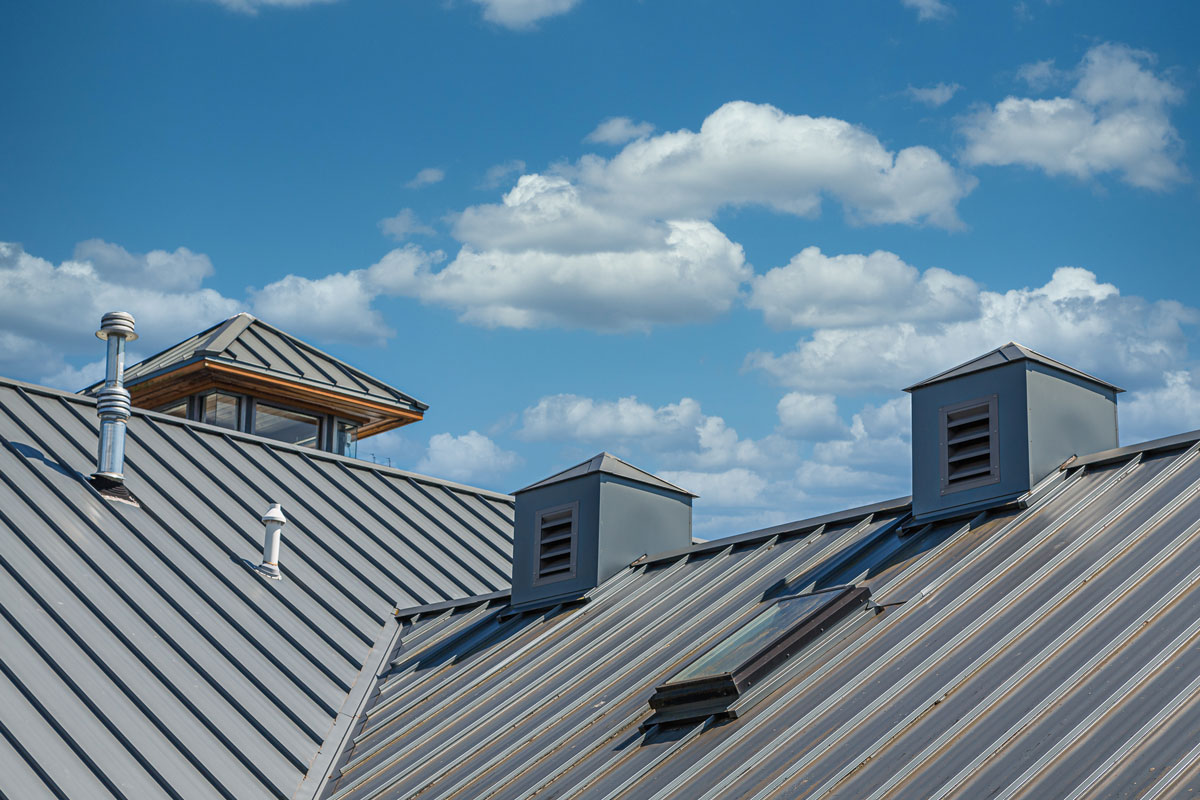 Gray colored metal roofing of a huge house with boot vents