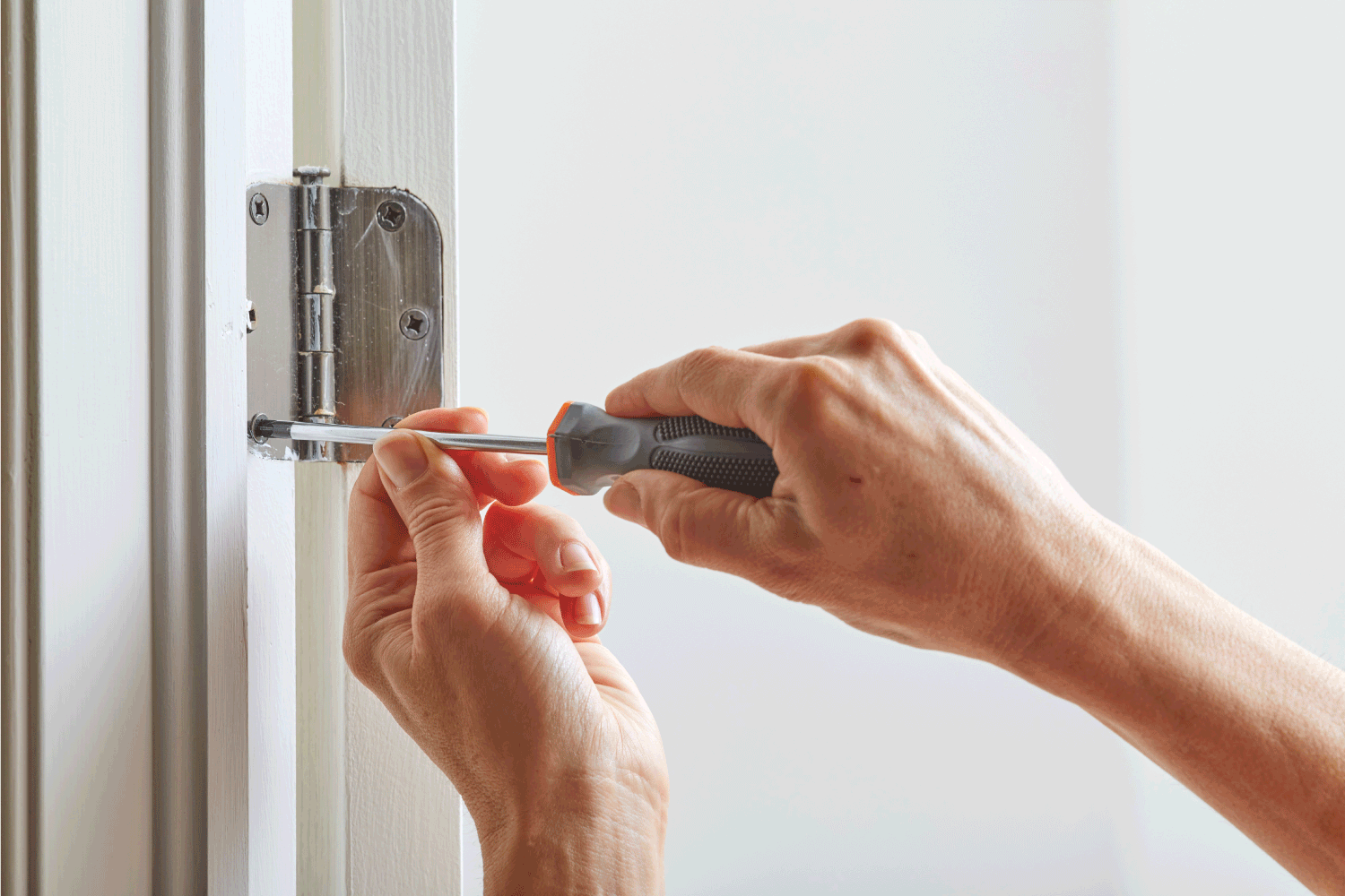 Hands with screwdriver fixing a door hinge.