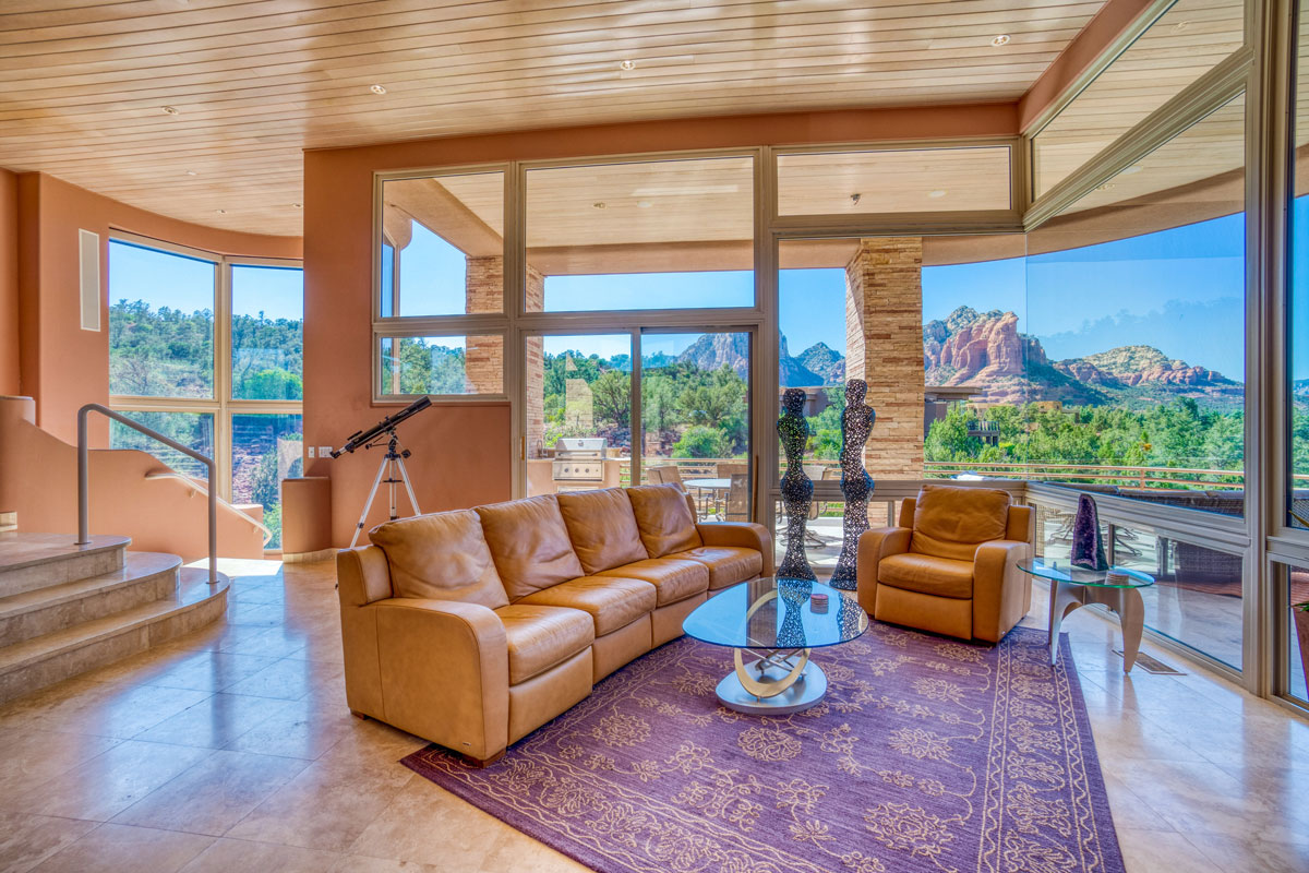 Interior of a two story mansion with leather sofa and matching tan painted walls with huge windows providing a scenic view of paradise landscape