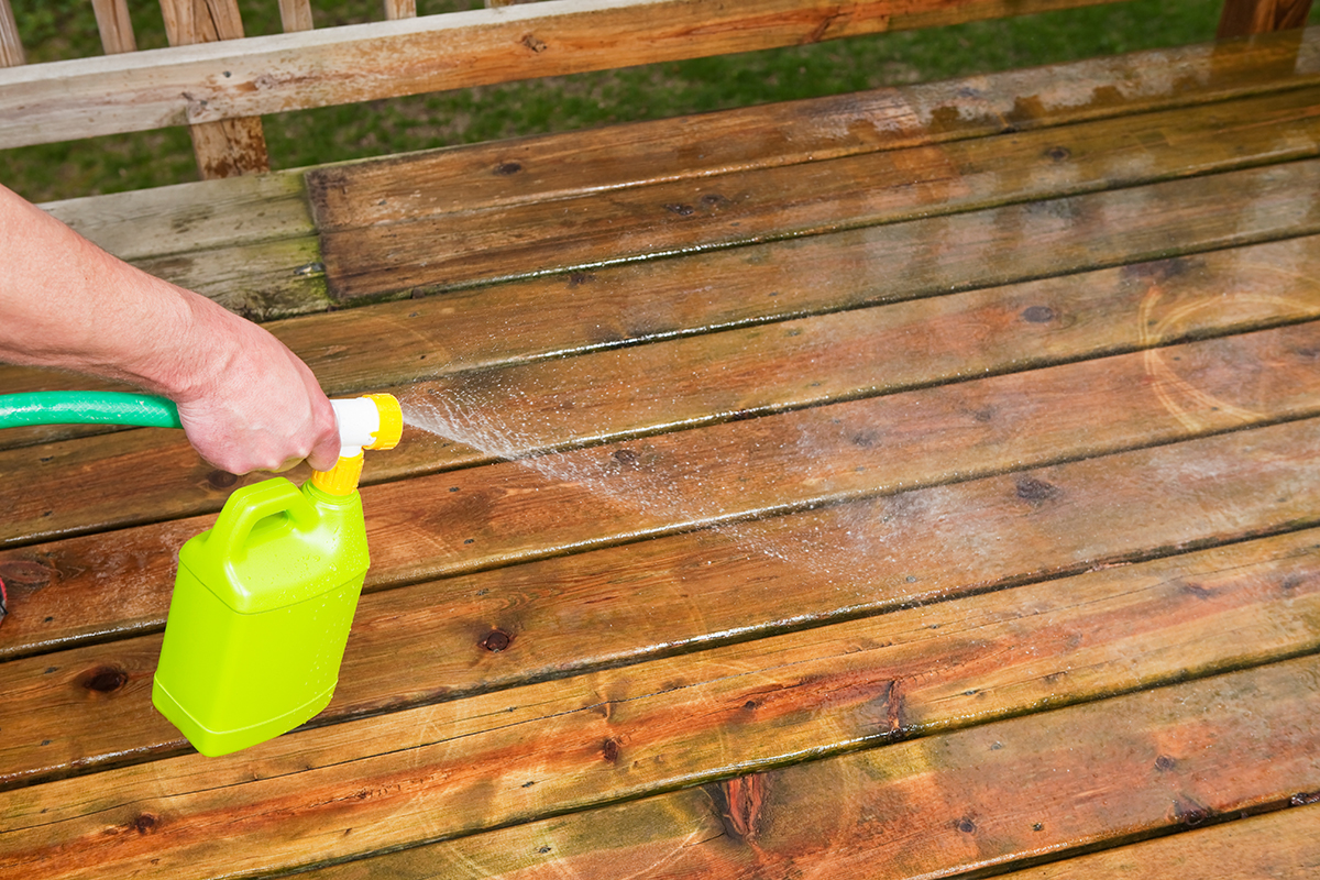 Liquid deck cleaner is being sprayed onto weathered boards which have been pressure washed