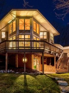 A luxury home with illuminated windows and a large composite deck in the woods, Should You Set Deck Posts In Concrete? [And How To]