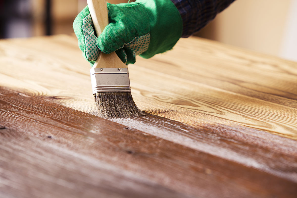 Man staining a big plank of wood for deck