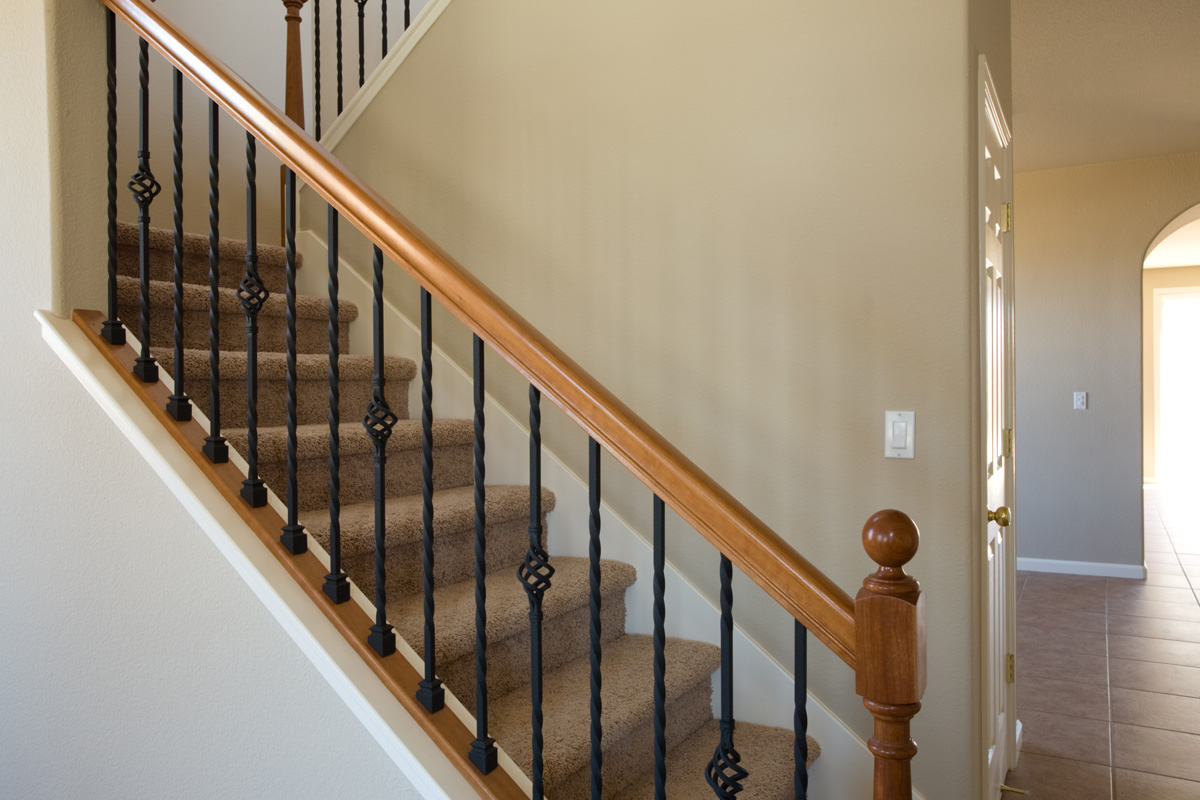 New residential home interior stairwell constructed of wood and iron with carpet steps.