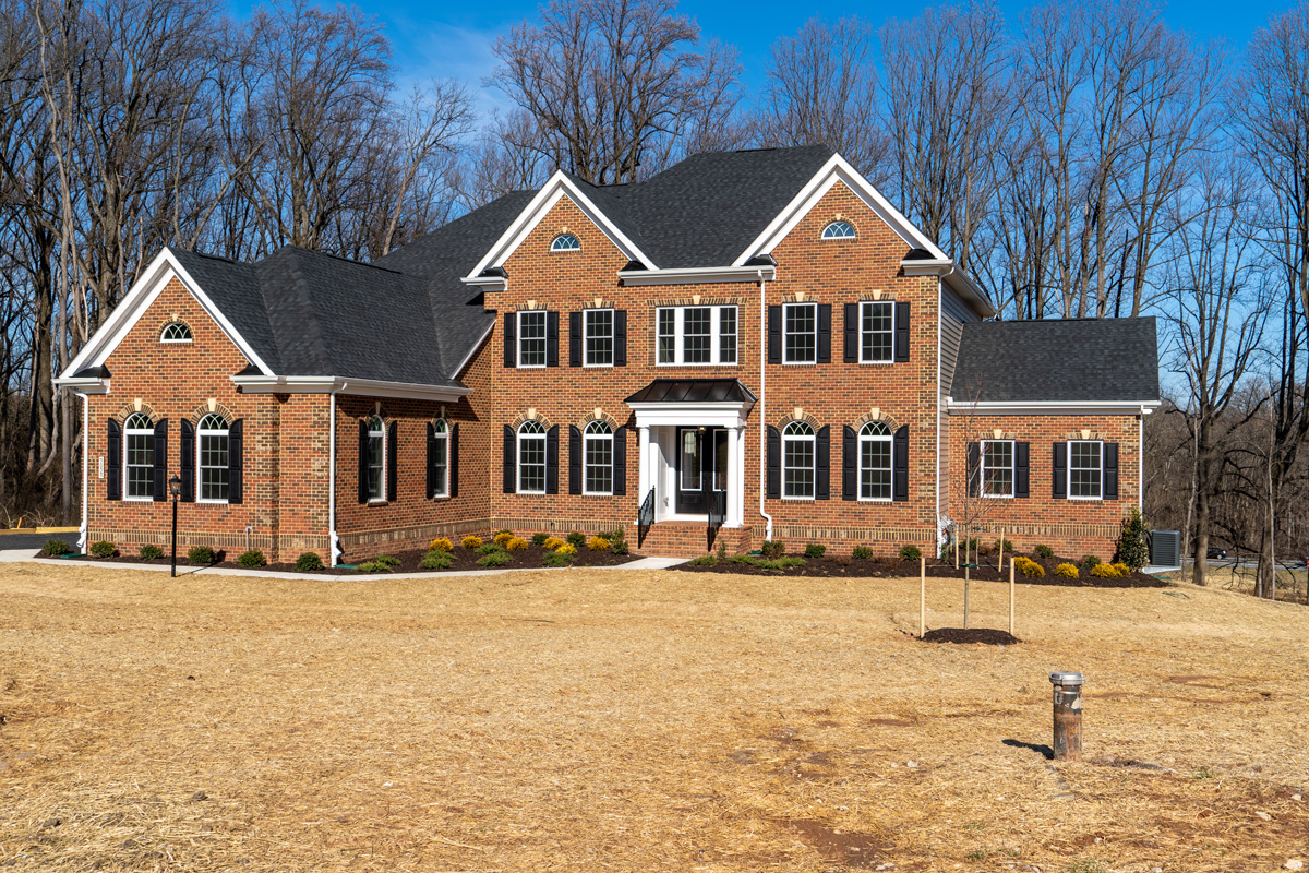 Newly constructed colonial mansion single family home, with brick facade, 2 peak gables, landscape, curb appeal, arched windows in a luxury neighborhood street in Maryland USA