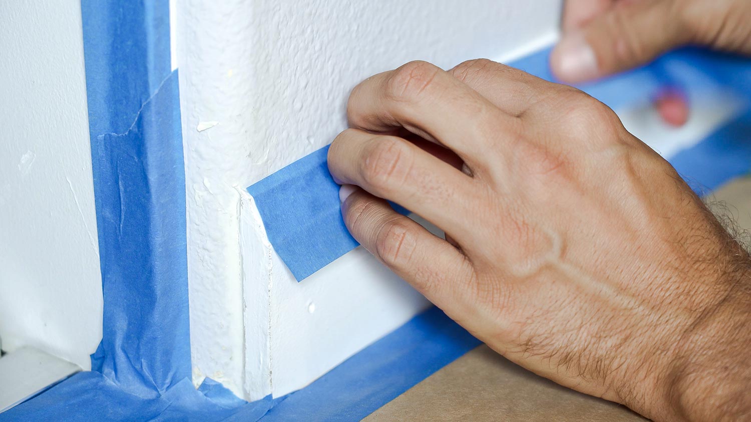 Painter using masking blue tape to secure baseboard