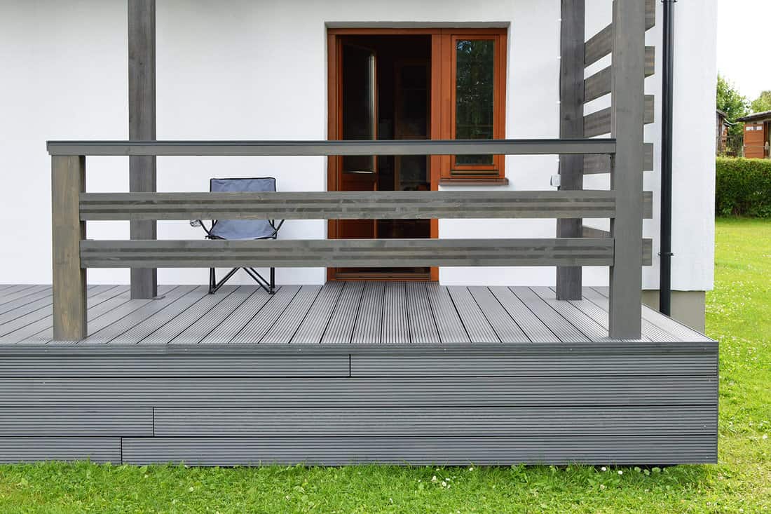 Part of white residential house with dark gray composite material terrace deck with wooden railings