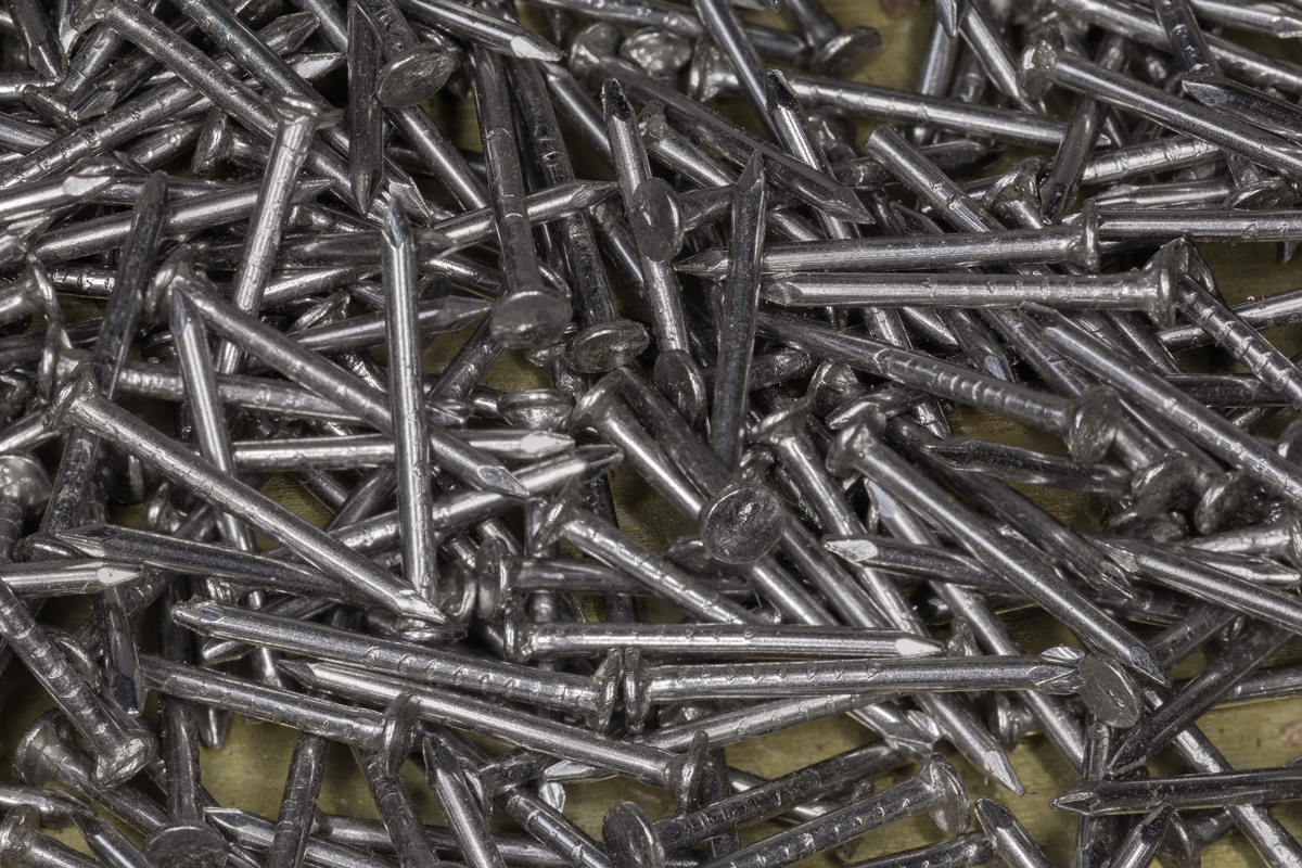 Pile of small steel nails with white anti corrosion coating, top view close-up in selective focus, background