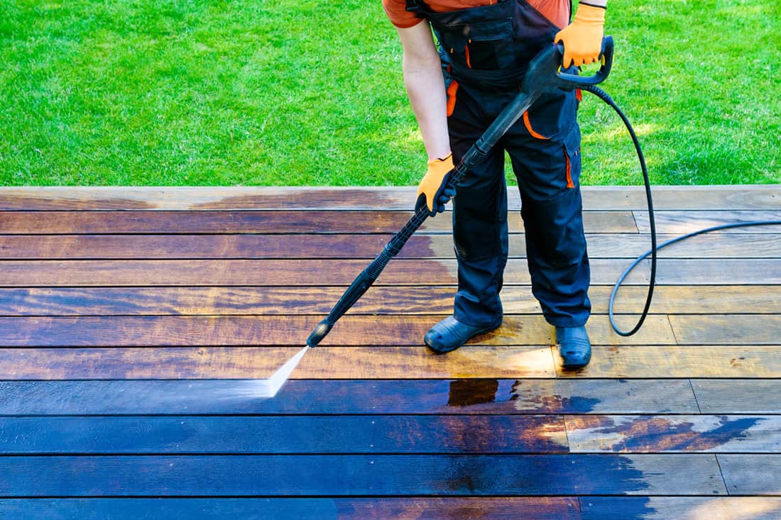 Power washing - worker cleaning terrace with a power washer - high water pressure cleaner on wooden terrace surface
