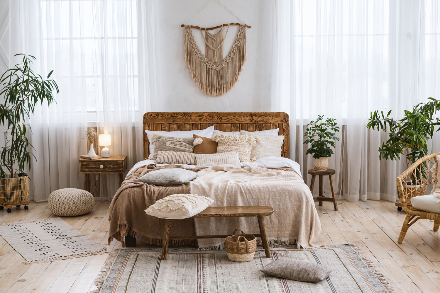 Rustic home design with ethnic decoration. Bed with pillows, wooden furniture, plants in pots, armchair and curtains on large windows in cozy bedroom interior, nobody, flat lay, panorama