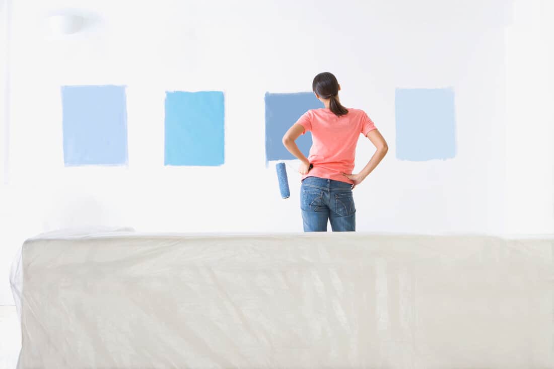 Rear view of a woman testing different paint shades over the wall.