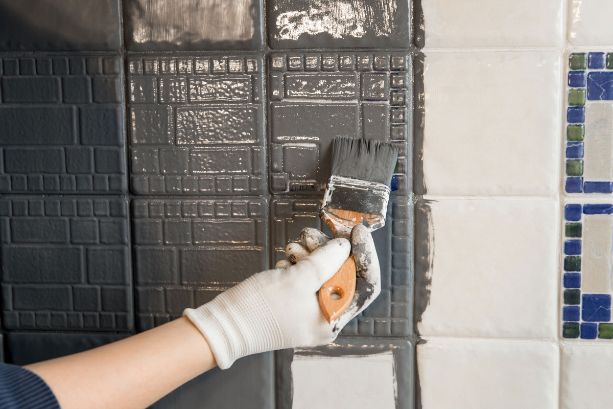 Repainting old dated kitchen ceramic tile back wall with modern gray chalk paint indoors at home