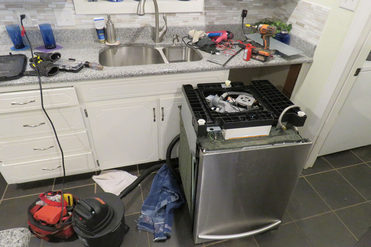 Repairing an old dishwasher under a gray countertop in the kitchen