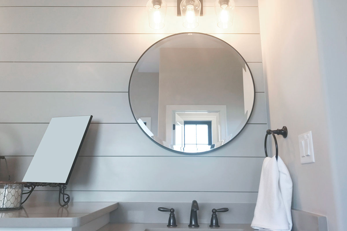 Shiplap Bathroom with big round mirror above the nickel type faucet and a facetowel in the right side of it
