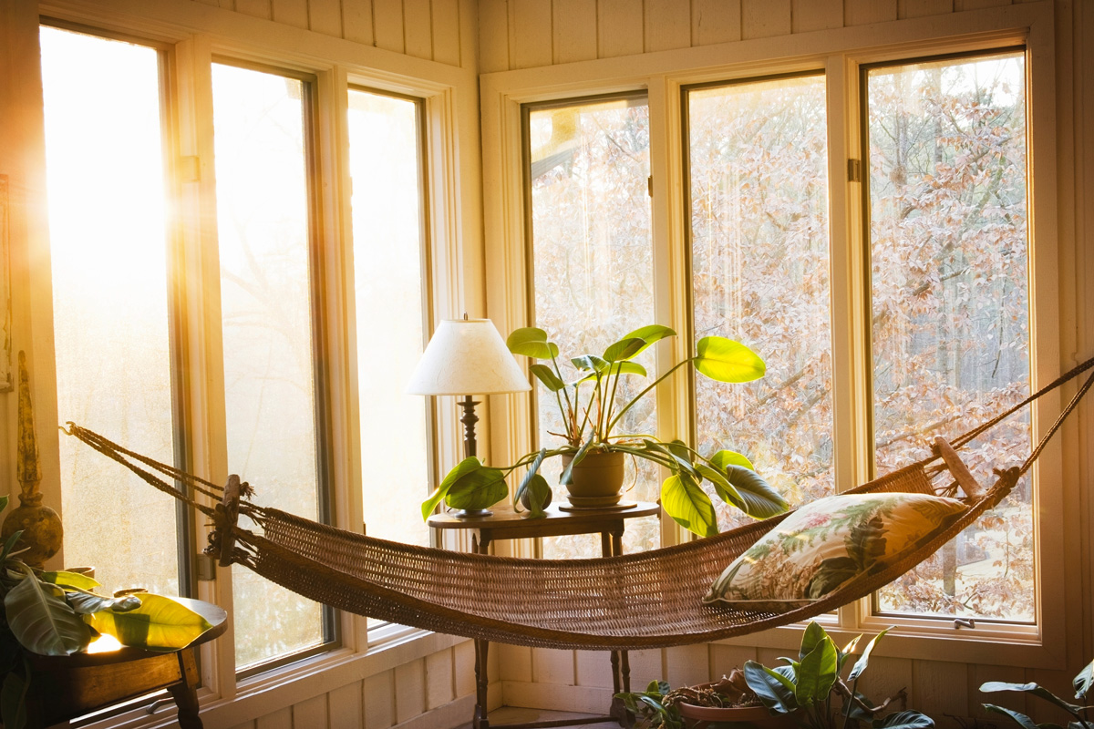 Sunroom with a wicker hammock and tall windows in the background. 