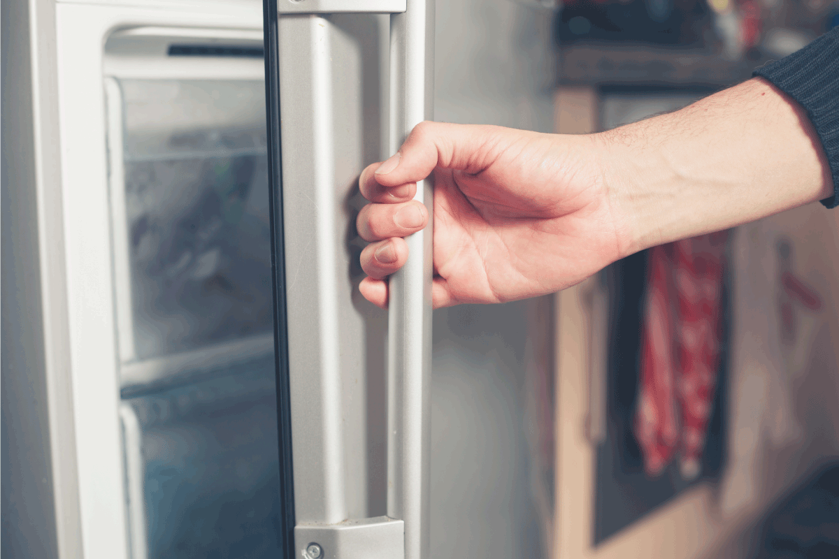 The hand of a young man is opening a freezer How To Find The Model Number On A Kenmore Refrigerator