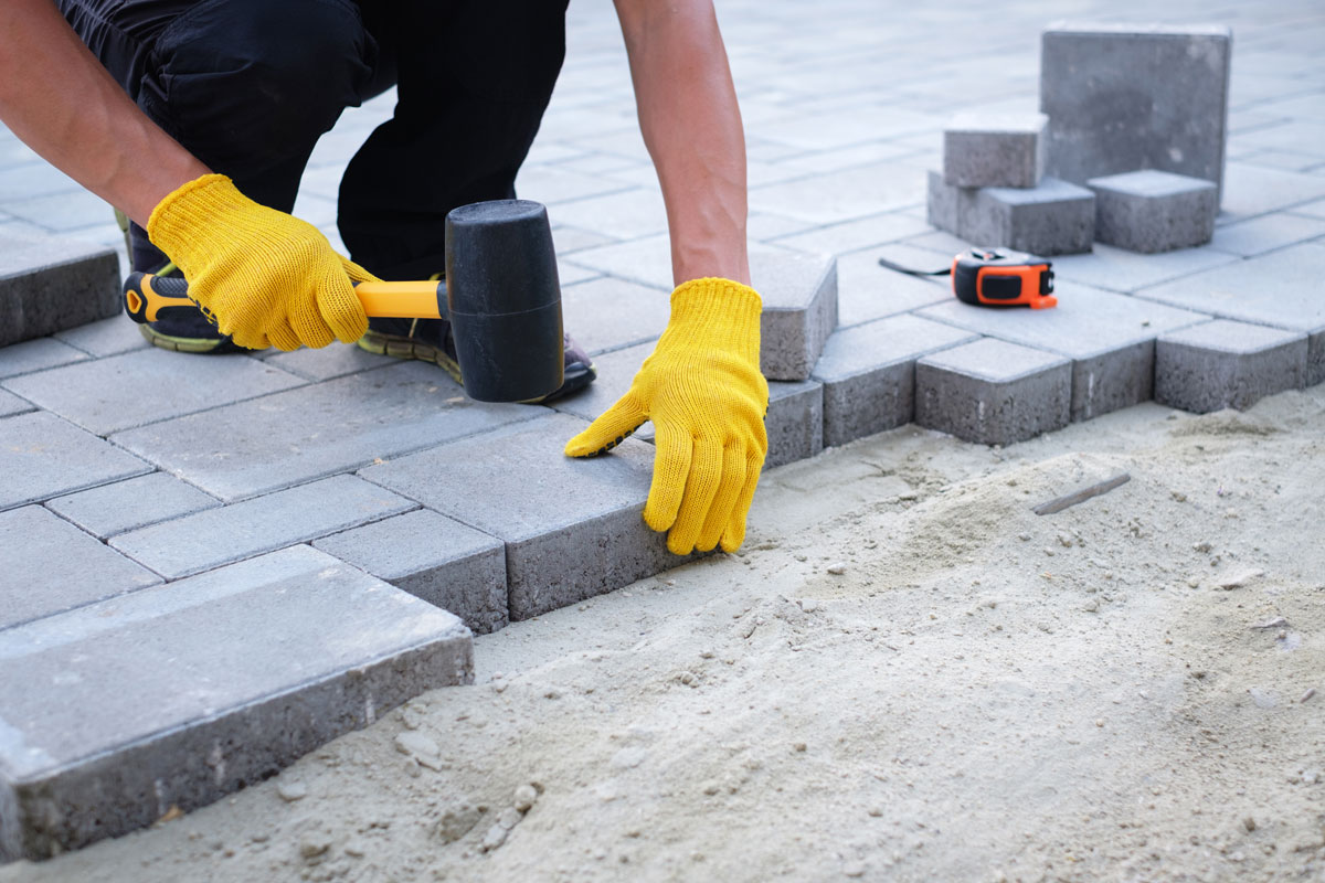 The master in yellow gloves lays paving stones in layers, Garden brick pathway paving by professional paver worker