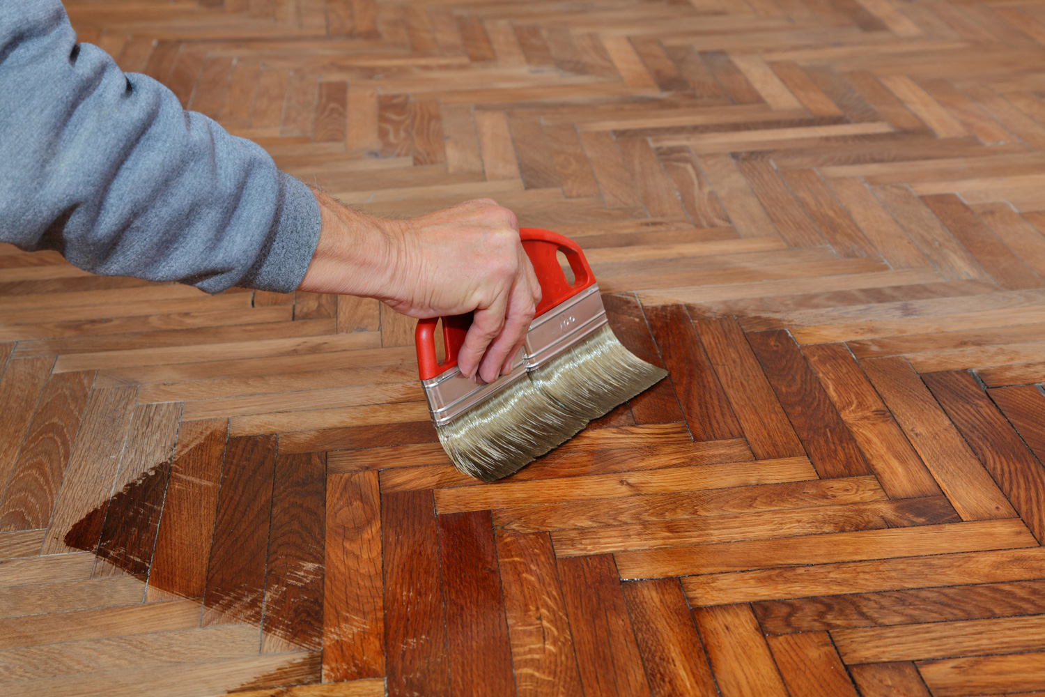 Varnishing of oak parquet floor, workers hand and brush