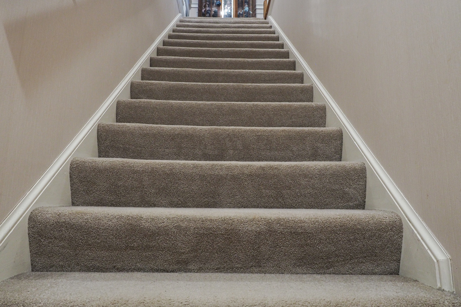 Wide shot low angle of of staircase up from basement in luxury house that is floored with baige color carpet with single wooden rail on the left