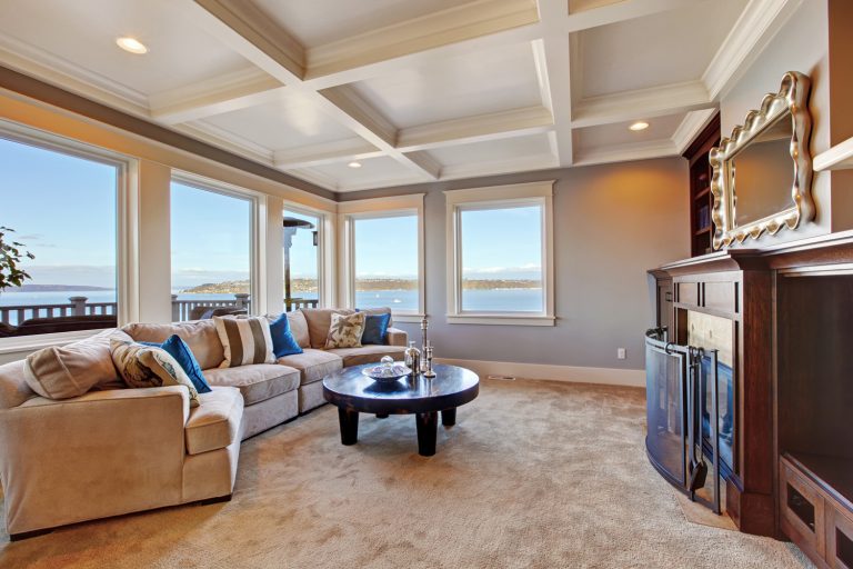 Warm living room interior with comfortable sofa, fireplace and coffee table. Room with coffered ceiling and soft brown carpet floor - Can You Add Or Remove A Tray Ceiling