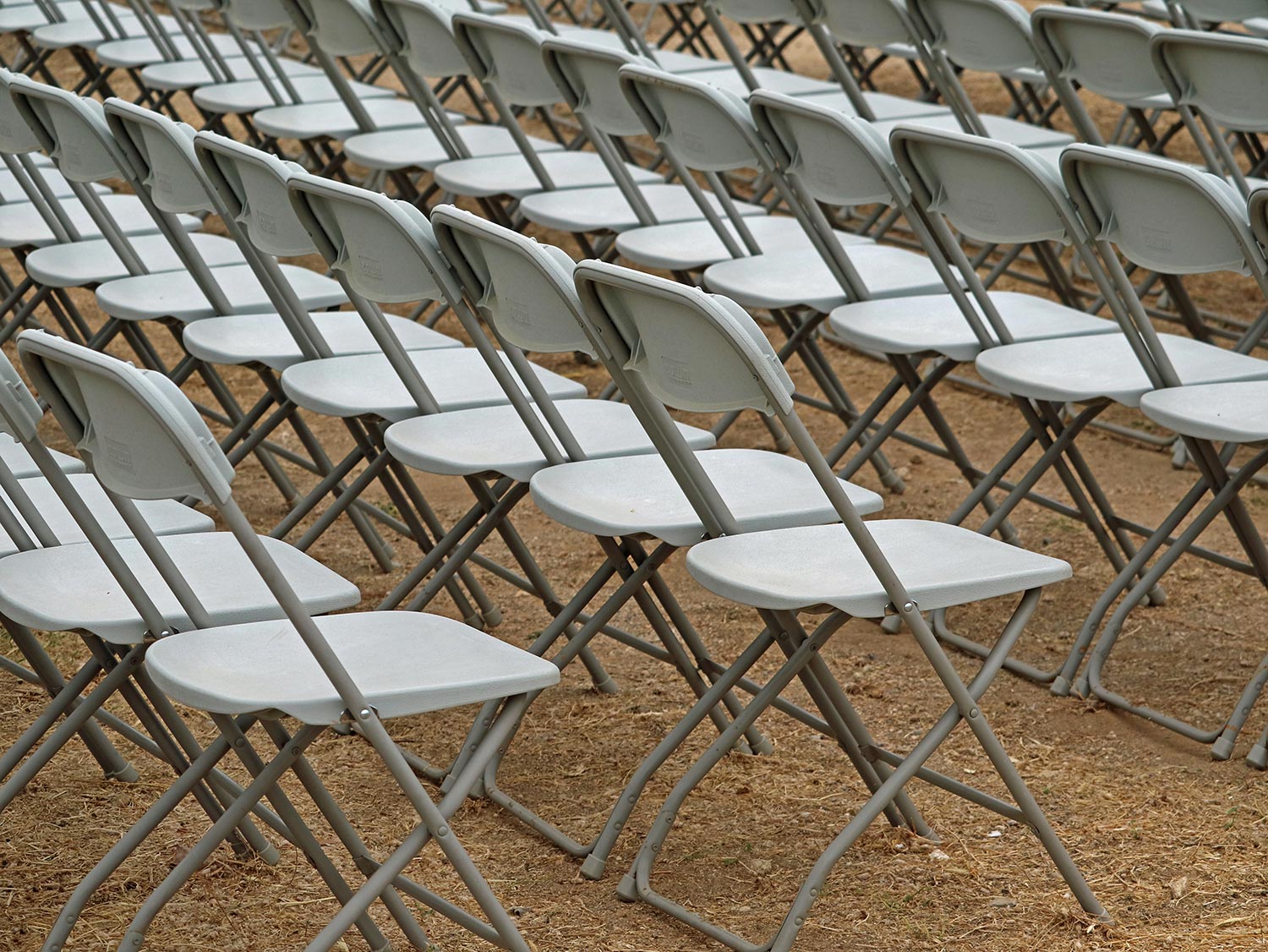 White chairs on sandy ground lined up for a presentation