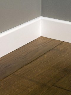 A white plastic plinths on dark wooden oak floor parque, How To Fill Gap Between Baseboard And Floor