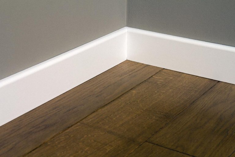 A white plastic plinths on dark wooden oak floor parque, How To Fill Gap Between Baseboard And Floor