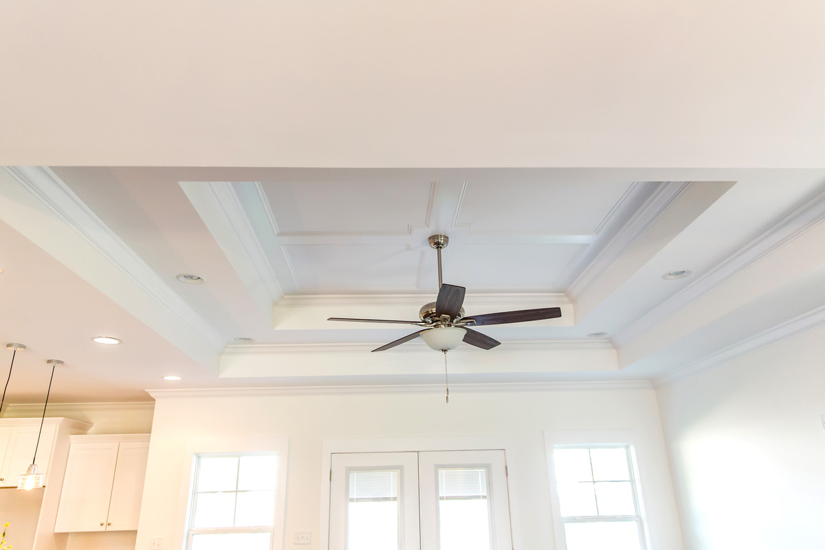 White tray ceiling in small new construction house with windows and a fan