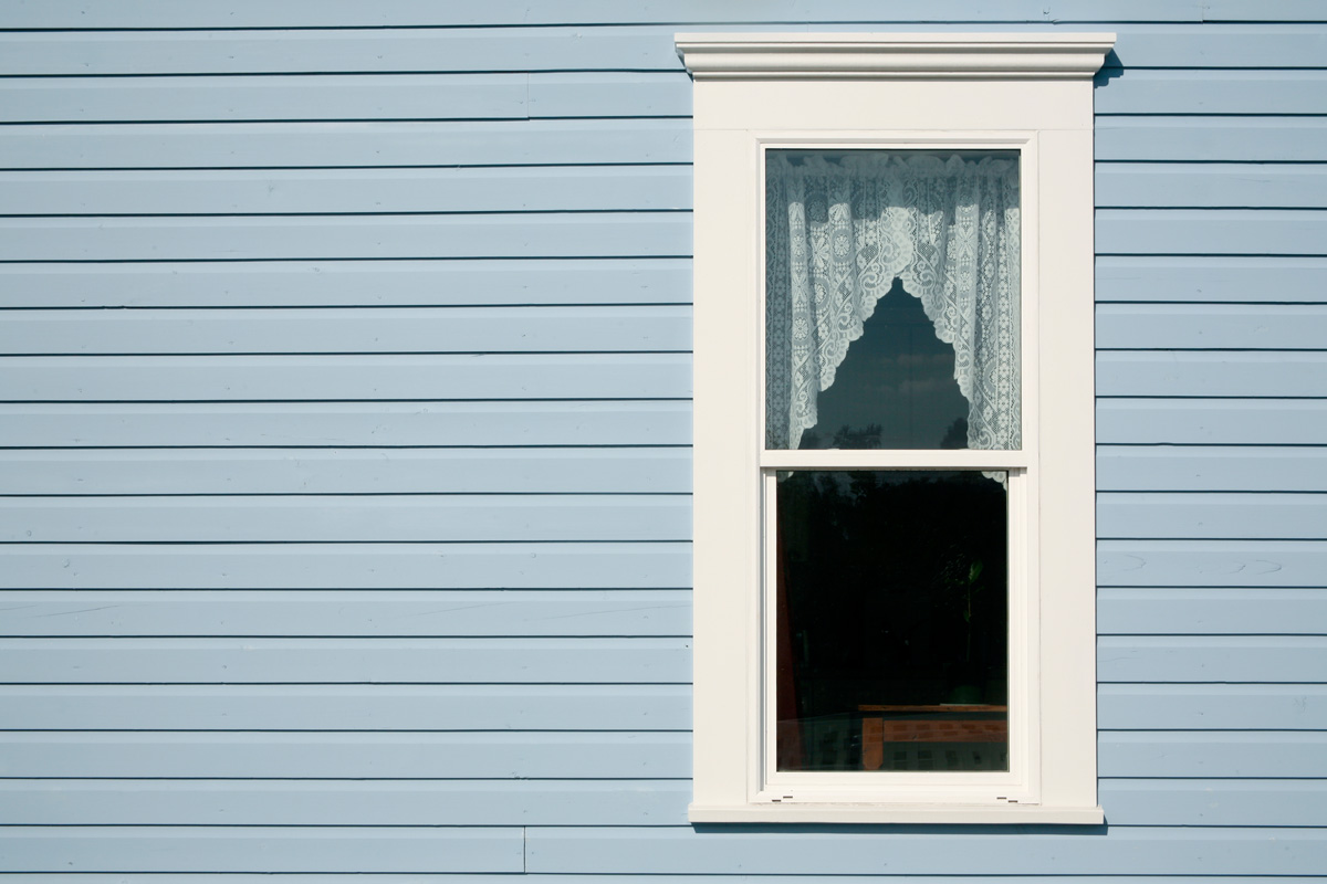 Window of a 100-year-old house. Antique lace curtains. Light blue wooden siding.