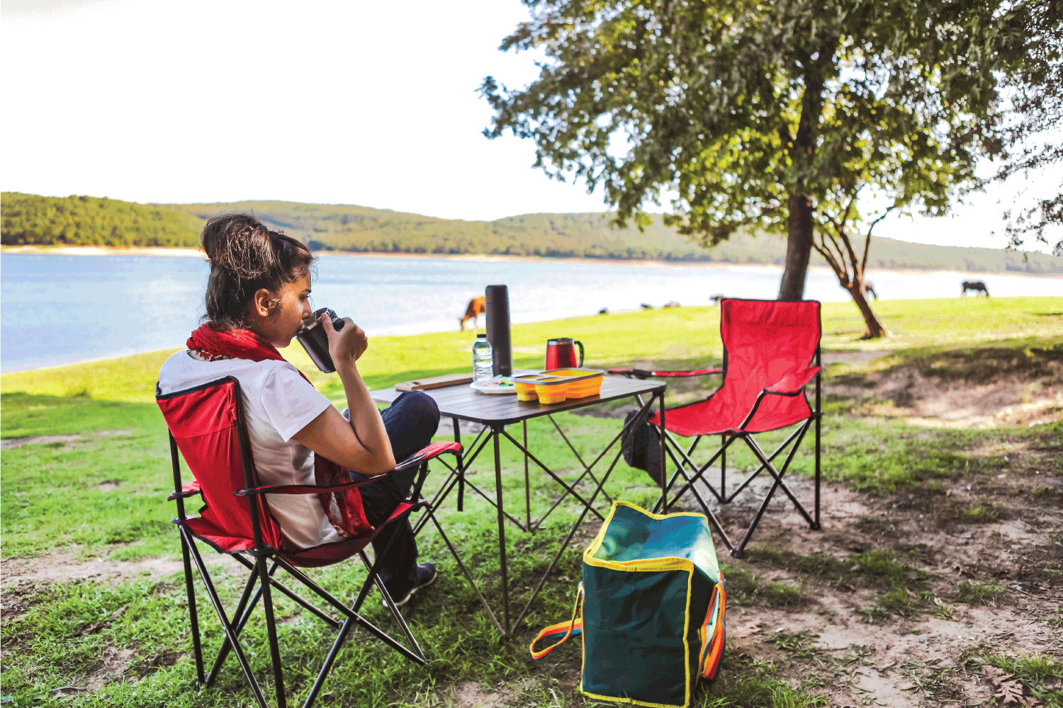 Woman drinking coffee while sitting on camping foldable chair