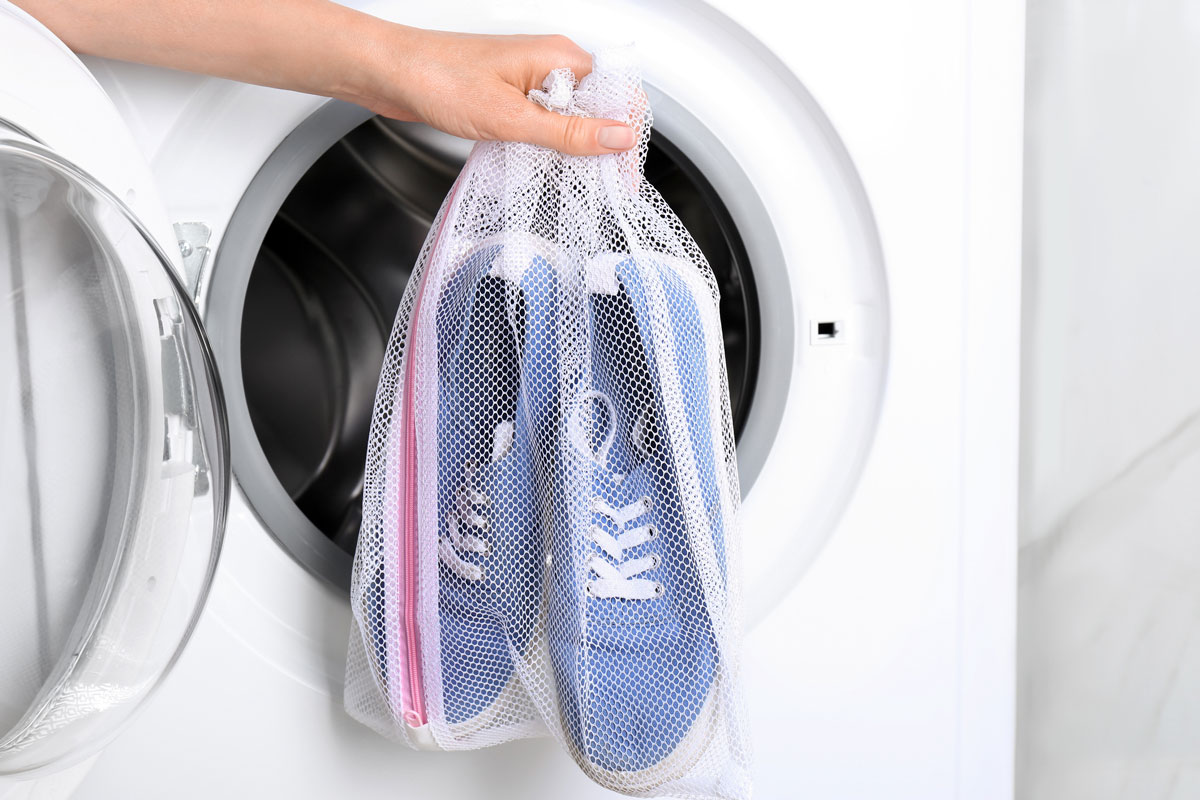 Woman putting pair of sport shoes in mesh laundry bag into washing machine