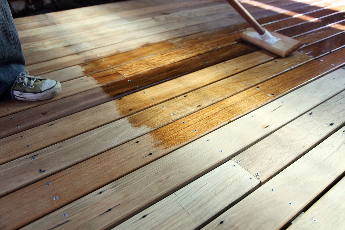 Worker using a mop to spread stain on the deck flooring