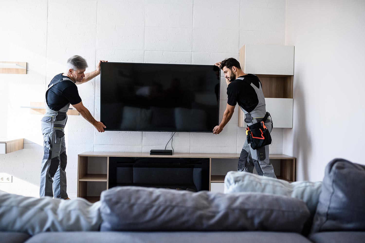 Workers in uniform installing television on the wall indoors