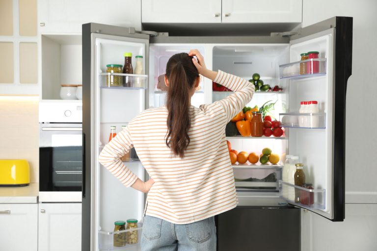 Young woman near open refrigerator in kitchen, back view, How To Find The Model Number On An Electrolux Fridge