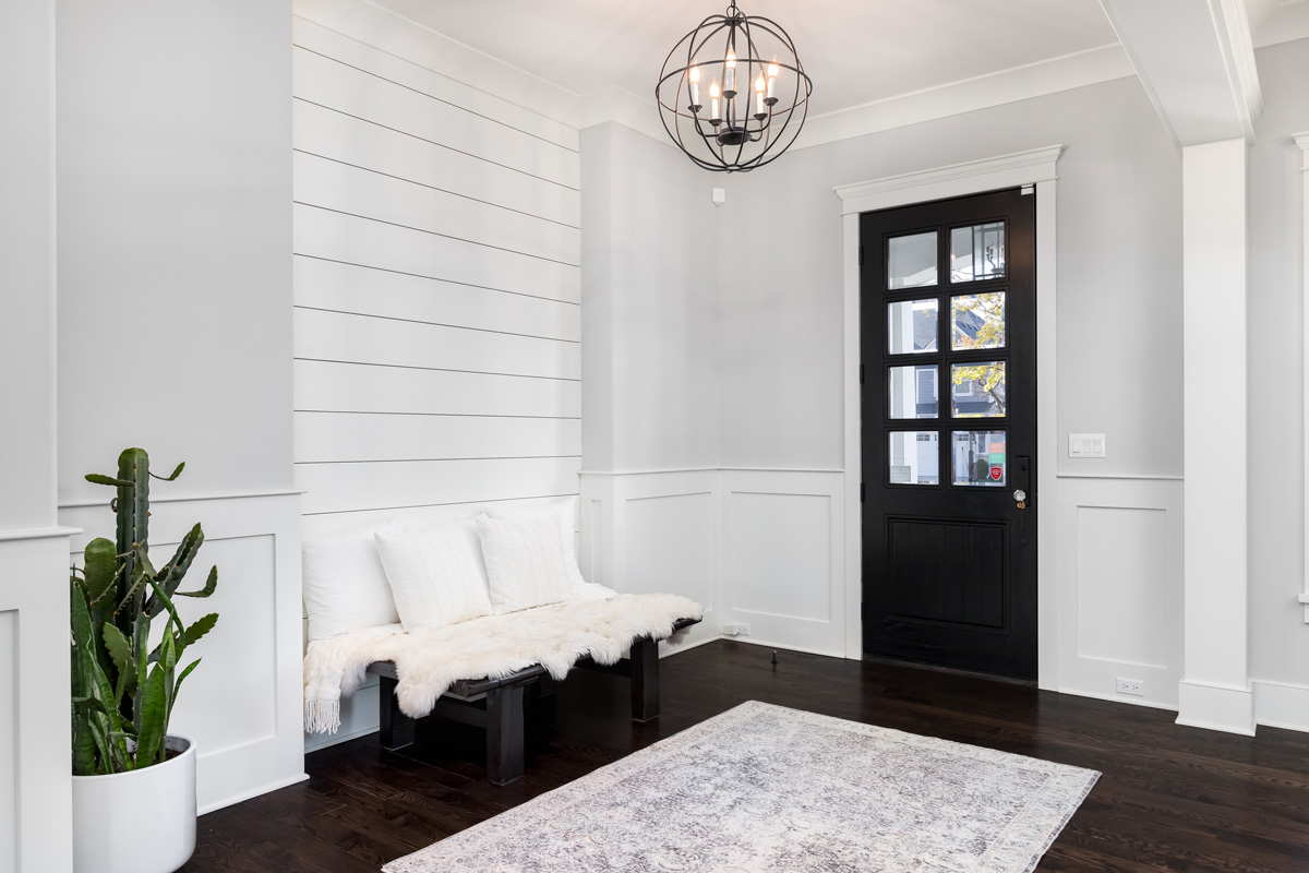  beautiful foyer entrance with a light hanging above the dark hardwood floors, a bench in front of a shiplap wall, and a dark door with windows.