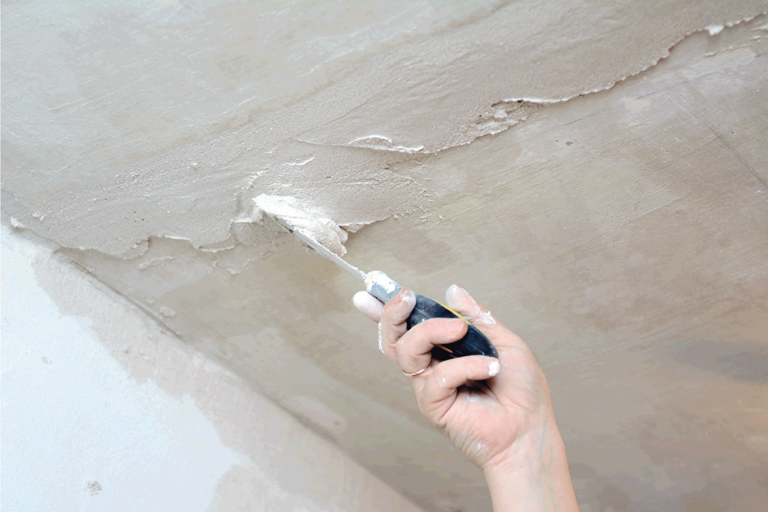 male hand holding a trowel on weight closing up cracks in the ceiling
