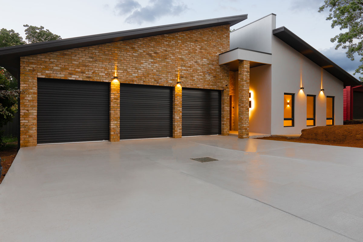 newly constructed single storey modern home showing a concrete driveway, triple garage doors, front entrance and large windows